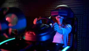 A woman experiencing a virtual reality driving simulator, wearing a VR headset while enthusiastically holding onto a steering wheel, bathed in ambient blue and red lights.
