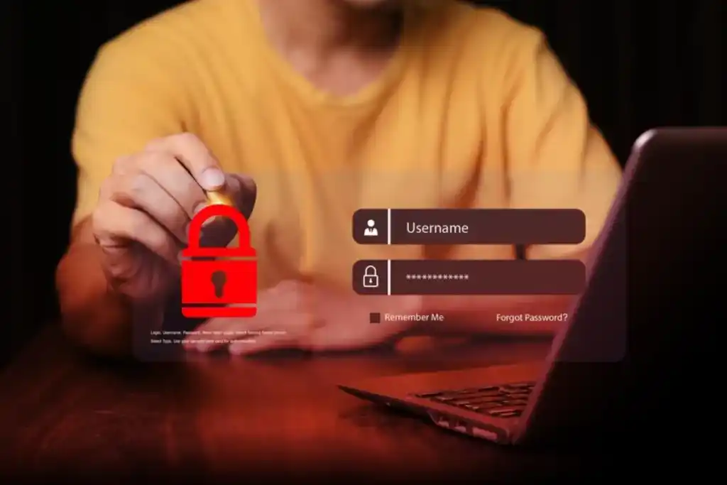 A person wearing a yellow shirt sitting behind a laptop with a login screen displayed, holding a digital red padlock symbol, symbolizing online security and data protection.