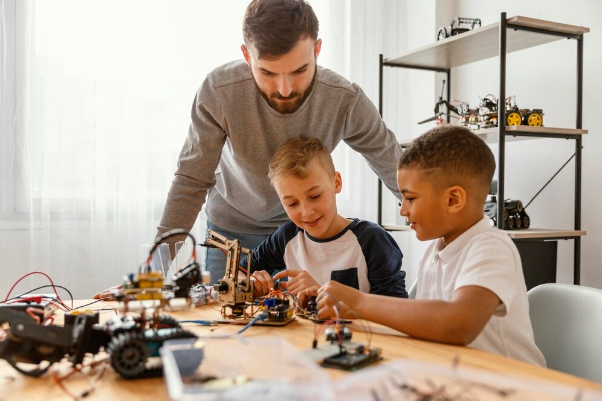 A group of children and an adult work on a robotics project, surrounded by tools and components on a wooden table.