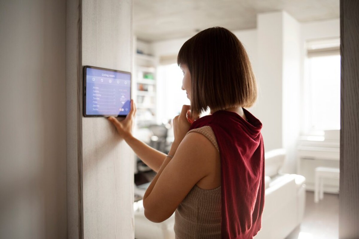 A person interacts with a sleek, modern wall-mounted touchscreen in a bright, minimalist living room.