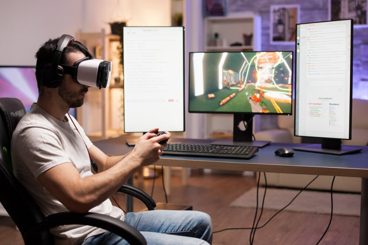 A gamer sits at a desk with multiple screens, wearing a VR headset and holding a controller, engaged in gameplay and community chat.