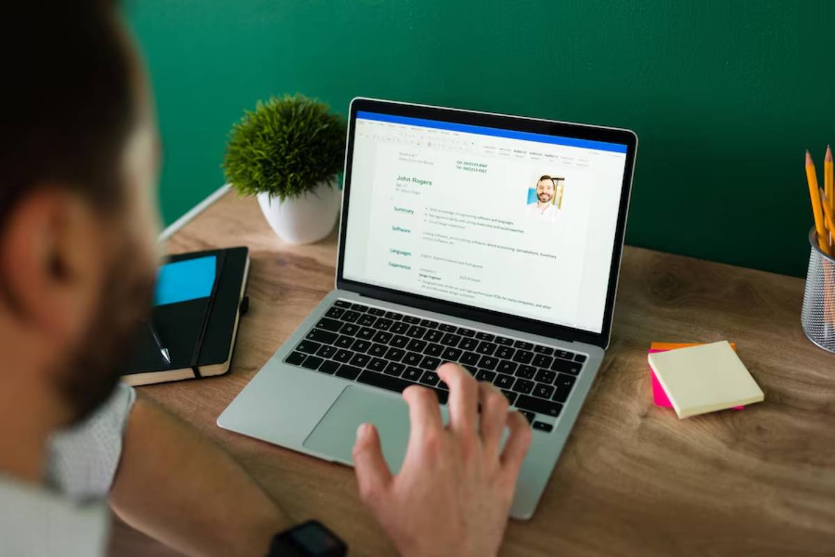 Man reviews a professional profile on a laptop in a home office setup with green wall background.