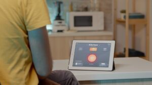 A person in a yellow shirt interacts with a tablet displaying smart home controls in a modern kitchen.
