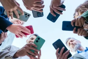 Low-angle shot of a diverse group of people holding smartphones pointed towards the center above their heads, indicating a social or technology-related gathering.