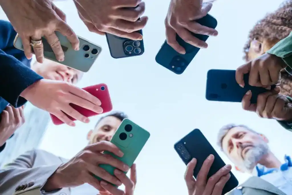 Low-angle shot of a diverse group of people holding smartphones pointed towards the center above their heads, indicating a social or technology-related gathering.