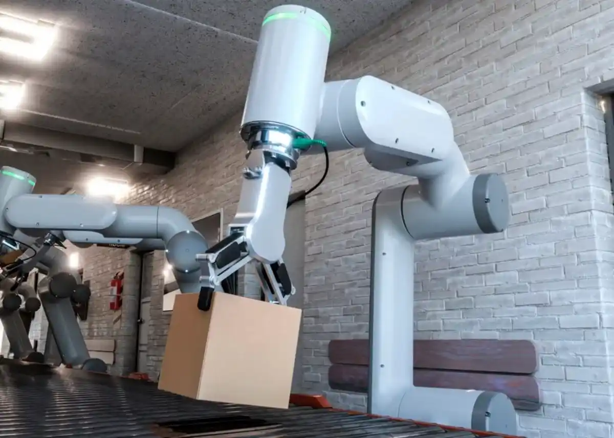 An industrial robotic arm lifting a cardboard box in a warehouse environment, showcasing advanced automation technology.